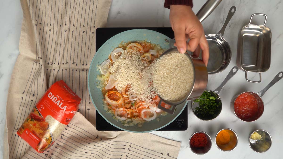 نُضيف أرز سيكالا المتوسط مباشرة إلى المقلاة ليمتص عصارة طهي الكاليمار والبصل.