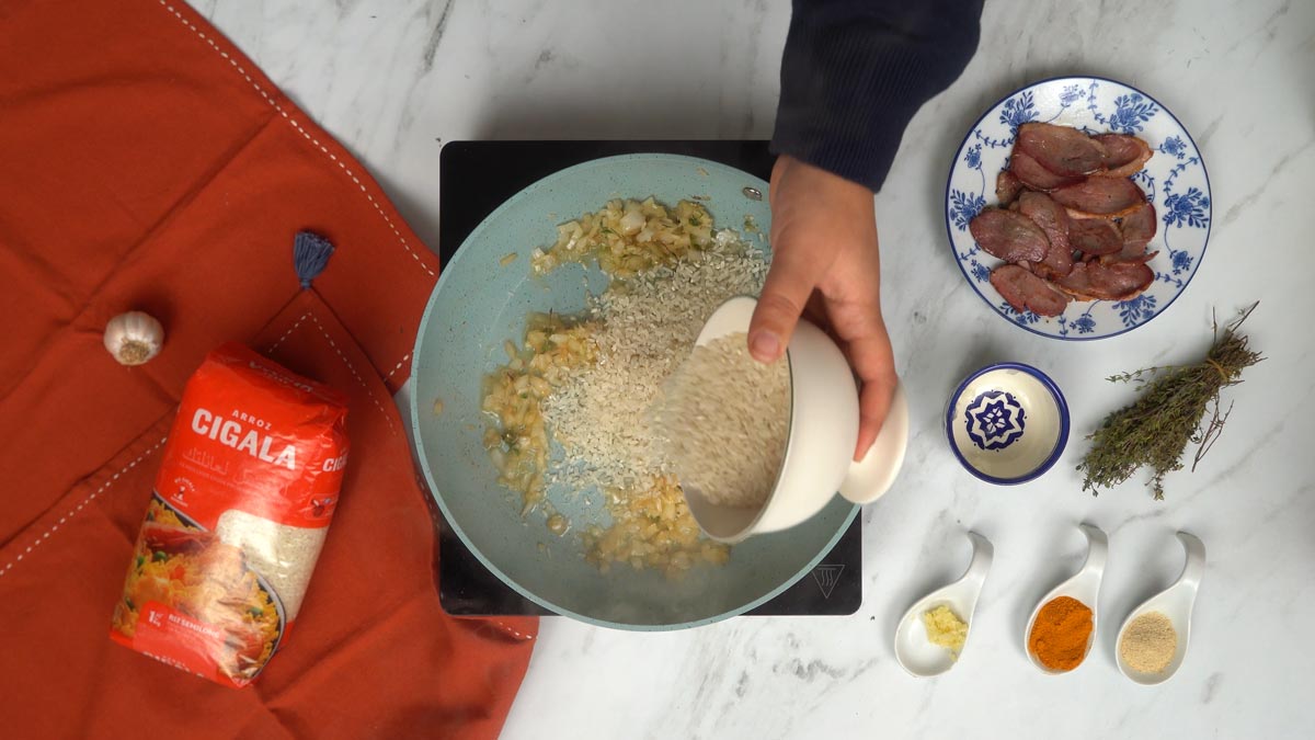 On verse le riz dans la poêle pour le nacrer légèrement avec les oignons et les arômes.