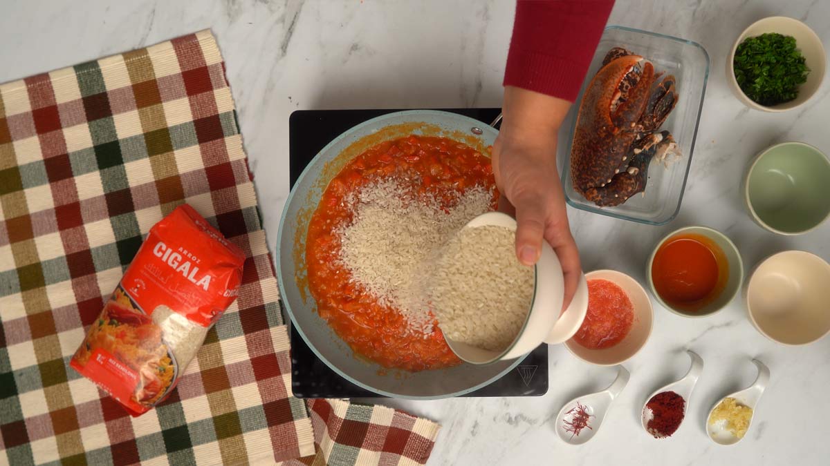 إضافة التوابل والأرز يُضاف الأرز النيّئ إلى المقلاة ليُقلّى قليلًا مع الخضار وصلصة الطماطم.