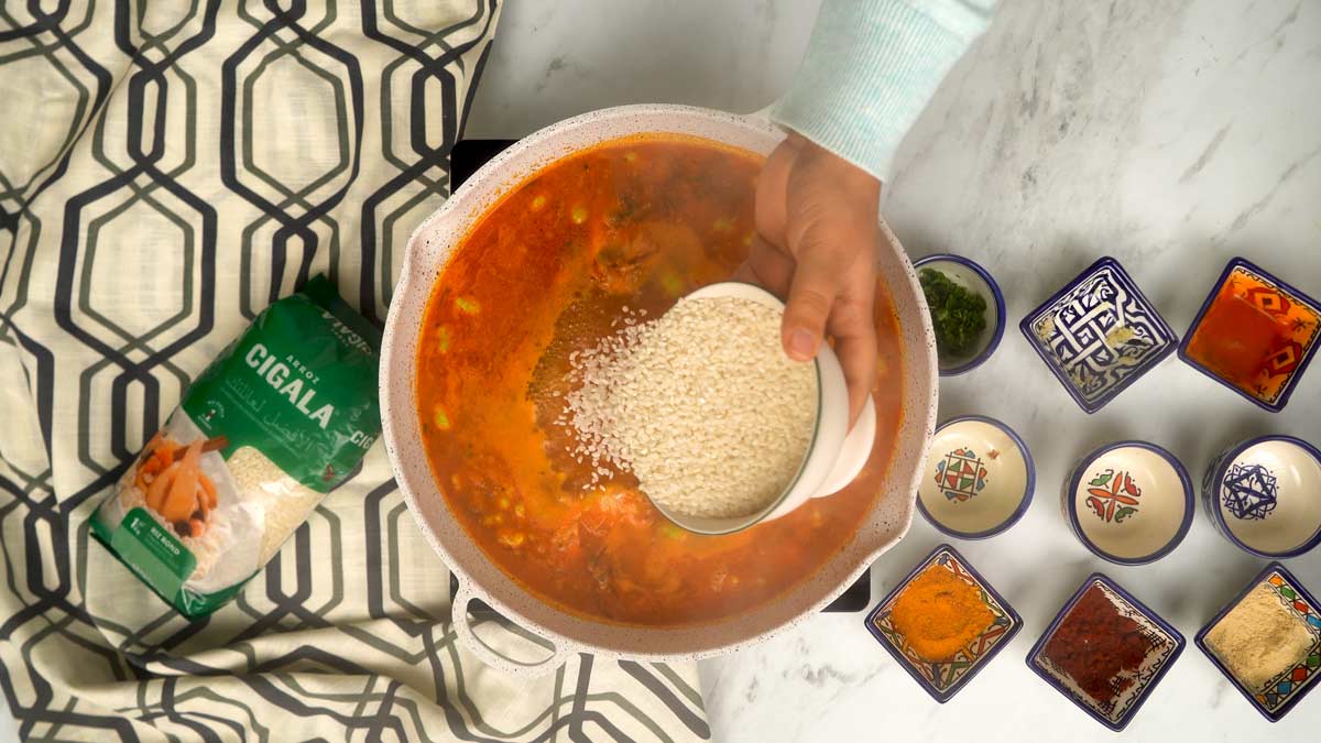 Le riz rond est versé sur le mélange de viande et de légumes déjà mouillé par le bouillon et les épices.