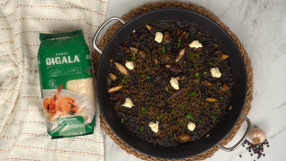 Le riz noir est servi directement dans la poêle, décoré de pointes d'aïoli crémeux et de persil.