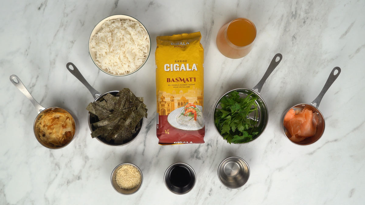 On prépare les ingrédients, notamment du riz basmati cuit, du saumon fumé, des lanières d'algues séchées, du persil, des flocons de bonite et du bouillon.