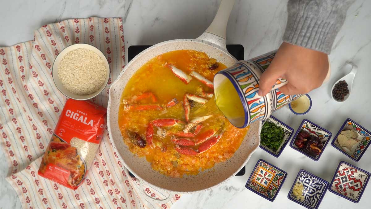 نضيف قطع السلطعون ونغمر المزيج بمرق غني لإتمام طهي الأرز.